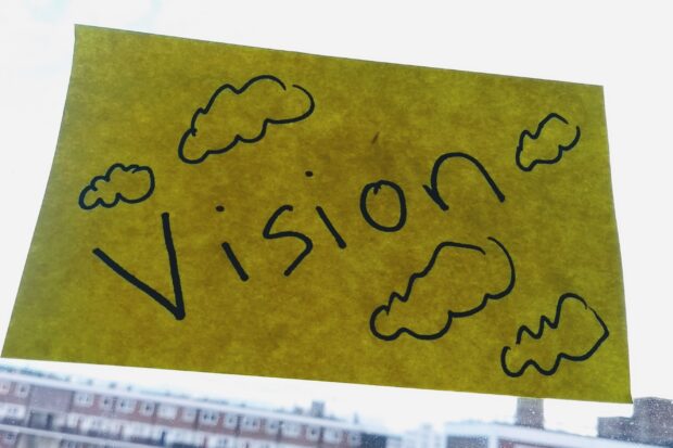 A post it note on a window with vision written on it and clouds around it.