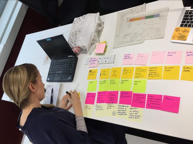 Claire, user researcher, analysing data using a laptop and sticky notes