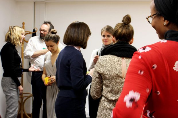 7 people standing up having a discussion in a meeting room