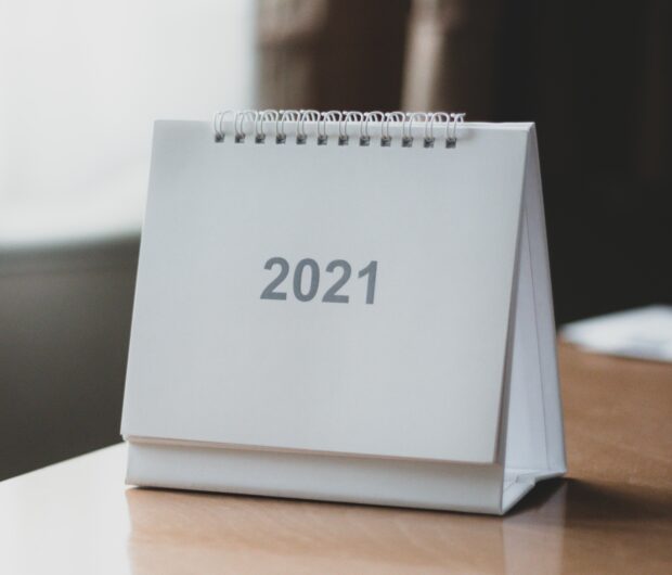 A small, white, spiral bound calendar that says '2021' in grey text, sat on a table.